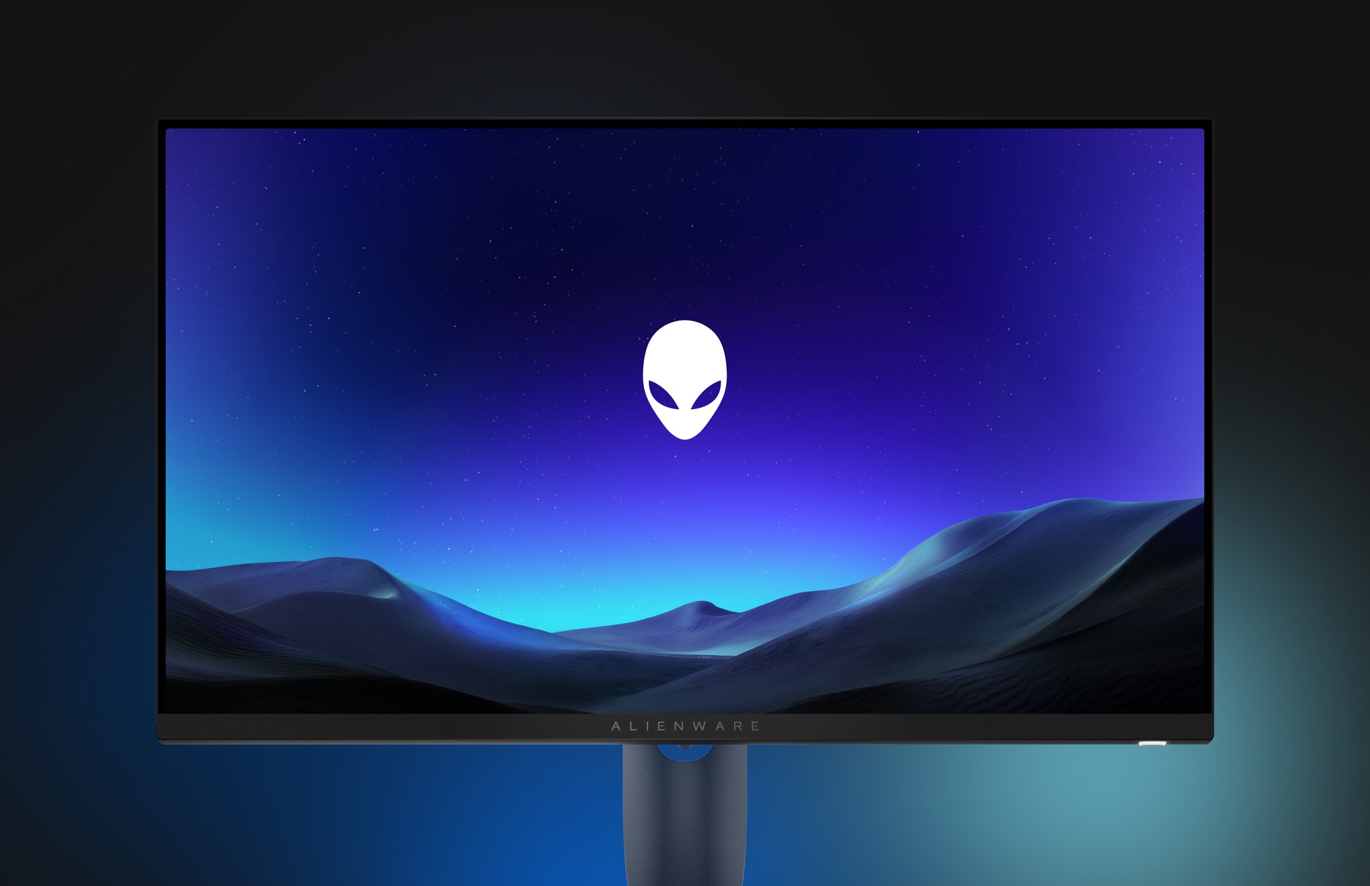 An Alienware monitor showing the alien head logo over a starry purple sky and blue sand dunes.